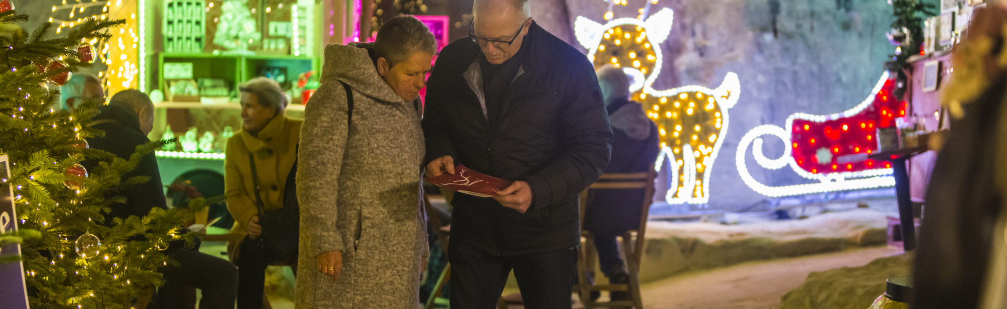 Ouder koppel kijkt op stratenplan brochure in een versierde kerstgrot